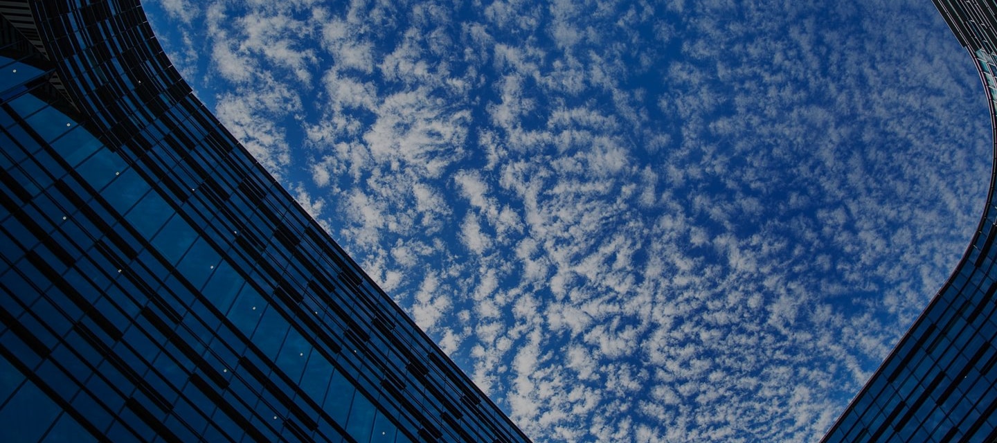 A skyward view framed by modern glass buildings with scattered clouds in a vibrant blue sky.