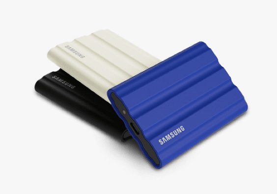 There are three Portable SSD T7 Shield. The Portable SSD in black and the beige are vertically lying on top of each other. The indigo blue Portable SSD is at a horizontal angle lying in front of the other two SSDs.