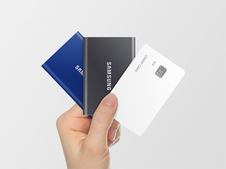 左からSamsung T7 の青色、グレー、白いクレジットカードの3つの製品を扇状に手で持っています。