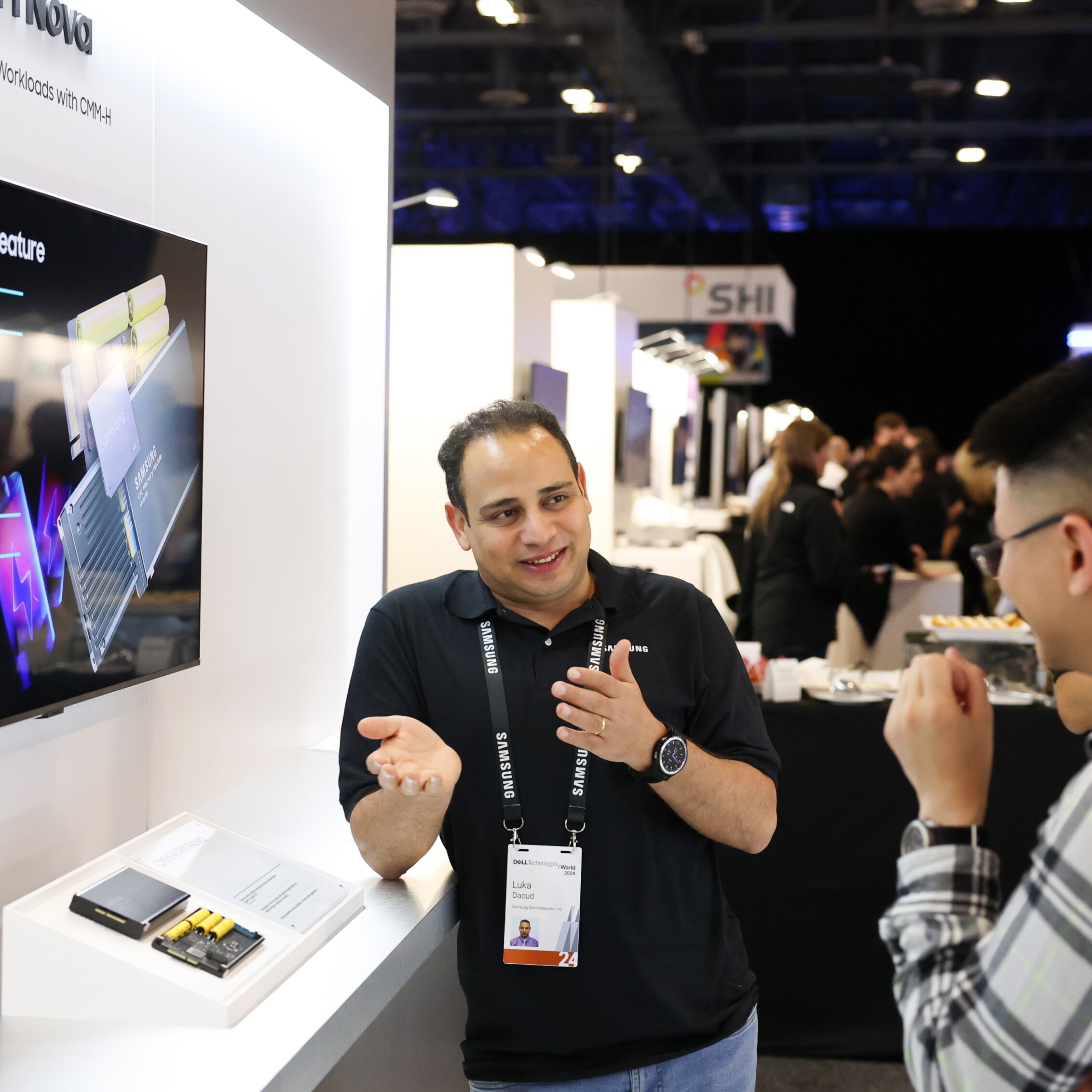 A technology expert at Dell Technologies World 2024 presenting Samsung Semiconductor products to a visitor, with a detailed screen display in the background.