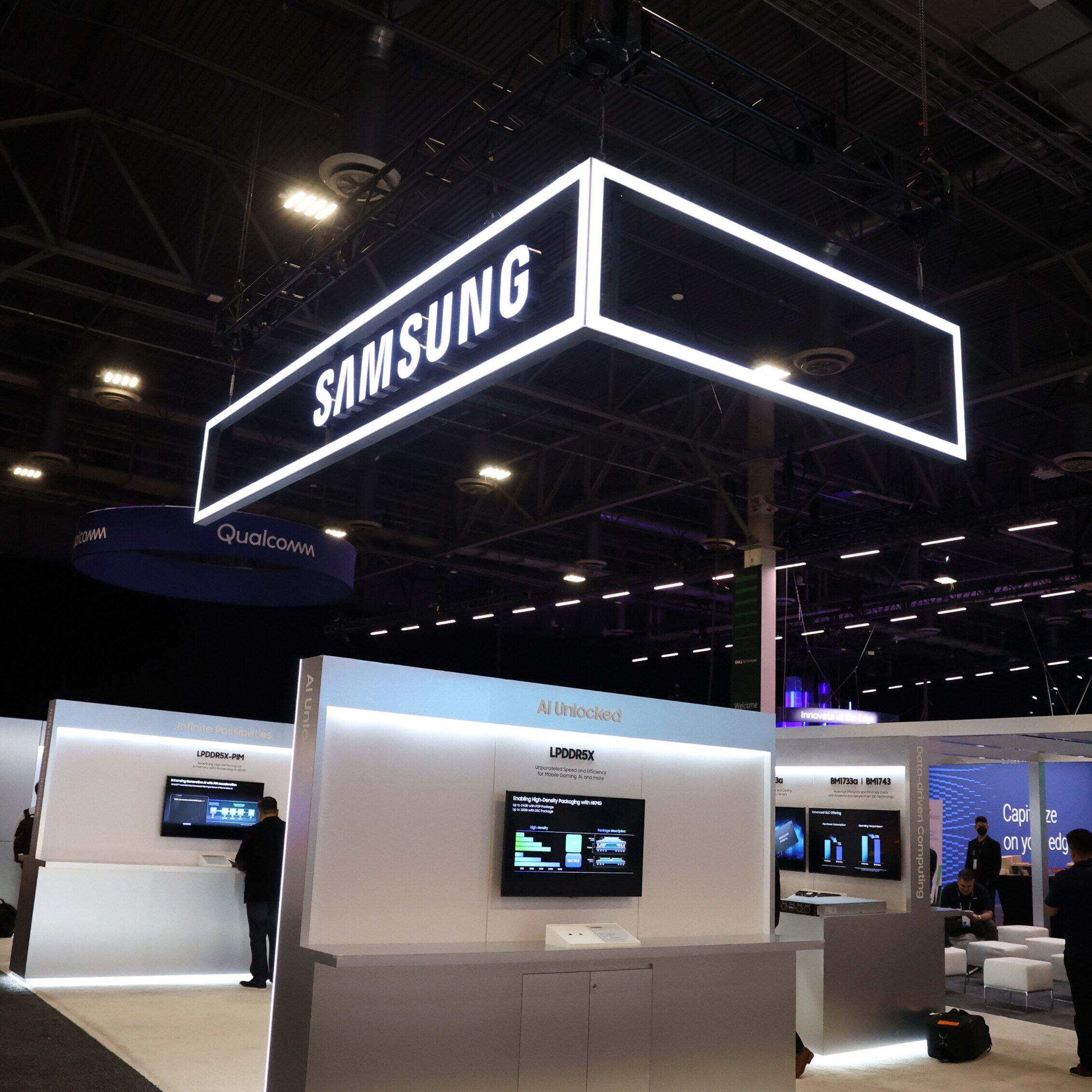 A vertical view of the Samsung exhibit at Dell Technologies World 2024, highlighted by an overhead illuminated sign and sleek display areas with interactive screens.