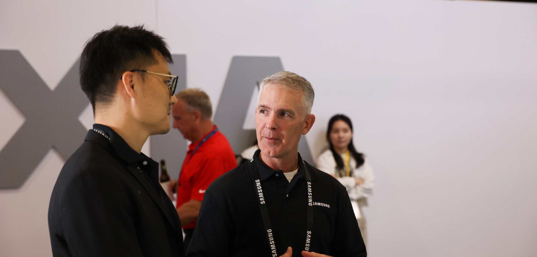 Two conference participants at Dell Technologies World 2024 having an in-depth discussion, with the event's signage and attendees in the background.