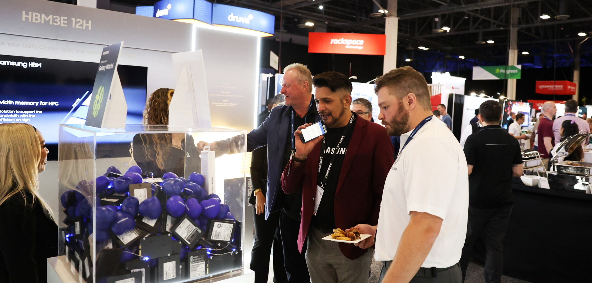 A group of attendees at Dell Technologies World 2024 gathered around a Samsung Semiconductor display featuring various products and informational screens.