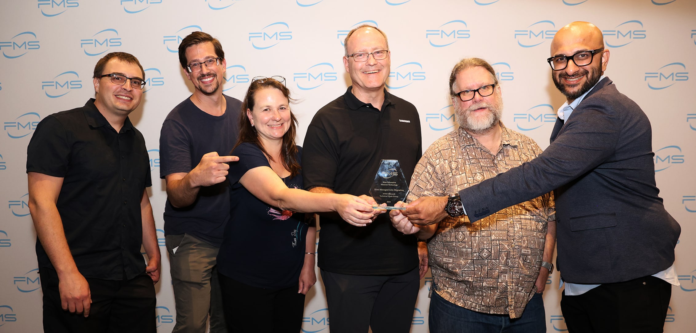 A group of six people smiling and holding an award together at FMS 2024 event.