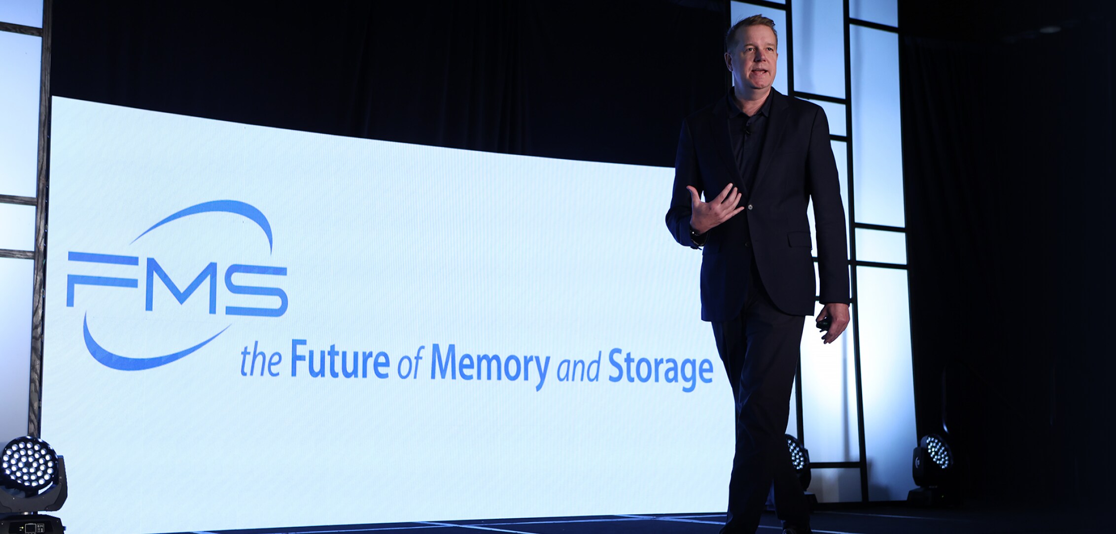 A speaker walking across the stage at FMS 2024, with a large screen displaying 'FMS: the Future of Memory and Storage' behind him.