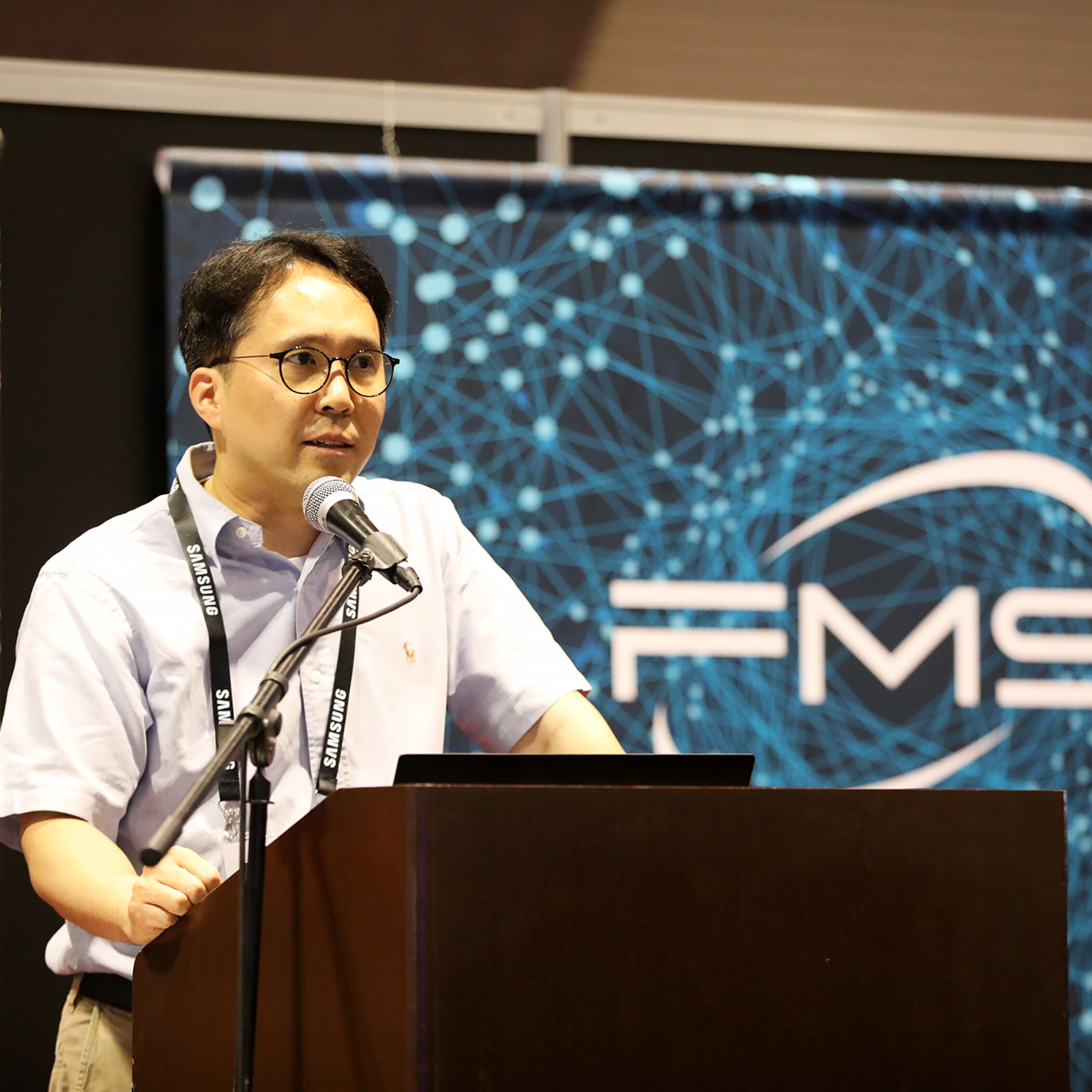 The speaker delivers a presentation at FMS 2024, with a backdrop displaying the FMS Tech logo.