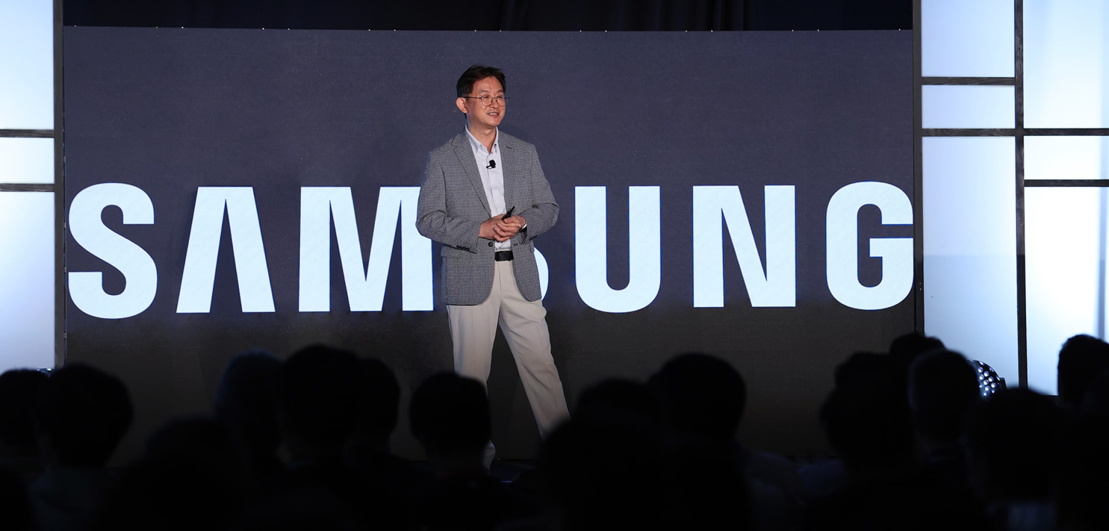 A speaker presenting on stage at FMS 2024, with a large screen displaying the Samsung logo behind him.