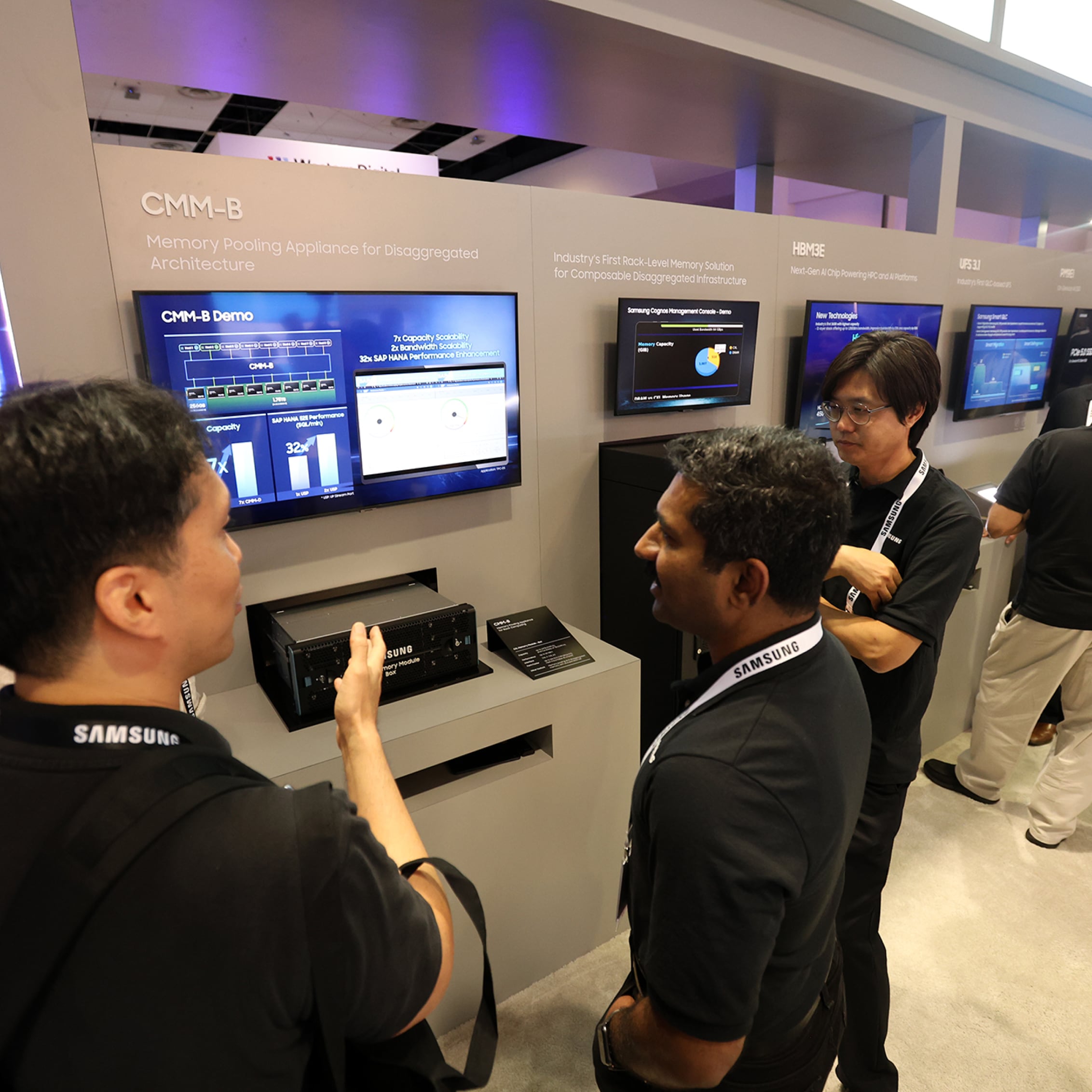 Attendees discussing in front of display screens showcasing Samsung's technology at FMS 2024 exhibition.