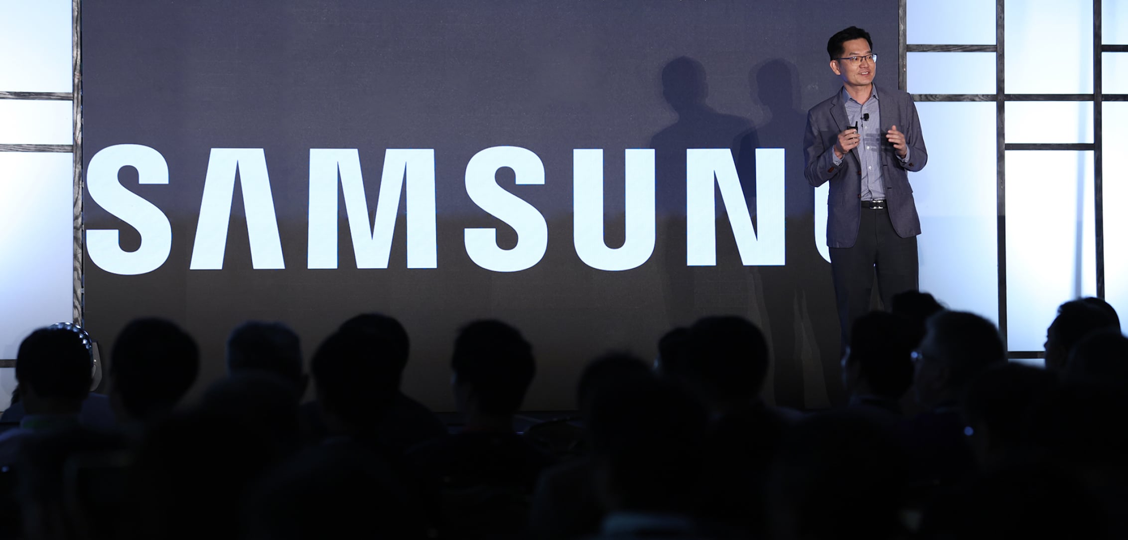 A speaker presenting in front of a large screen displaying the Samsung logo at FMS 2024, with an audience watching attentively.