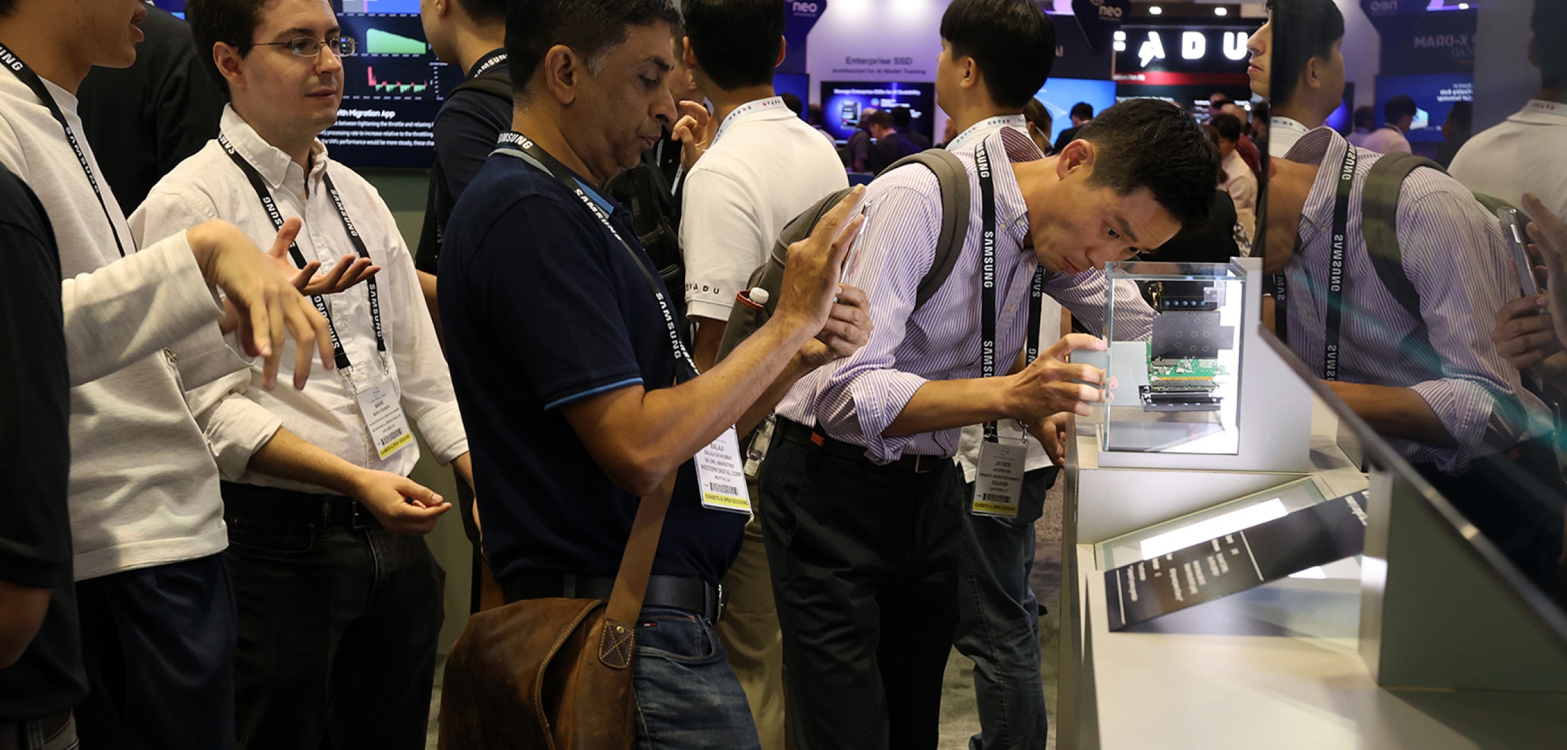 Attendees at FMS 2024 closely examining a technology display, with one person taking a photo of the exhibit.