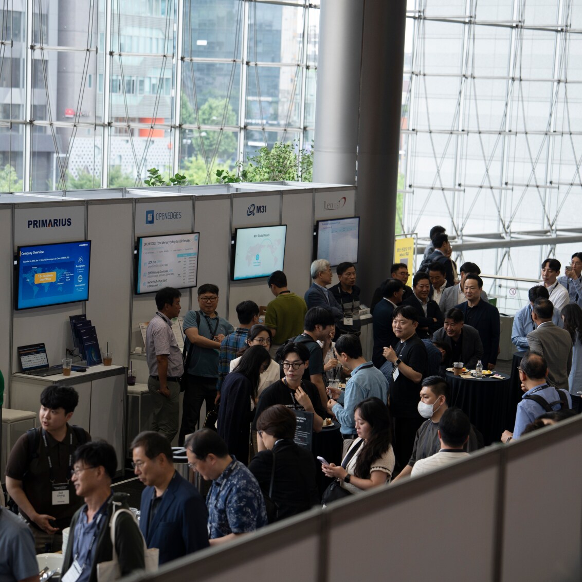 A bustling exhibition hall with attendees interacting at various company booths, featuring display screens and promotional materials.