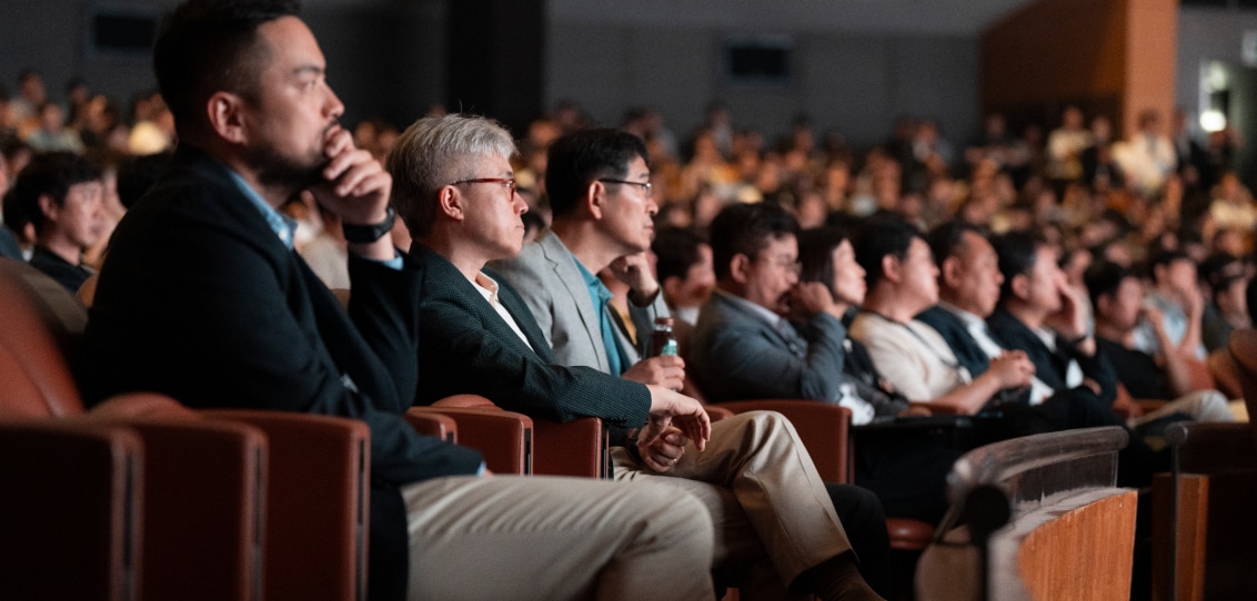 A group of professionals in an auditorium, listening attentively to a presentation, with a mix of expressions and attentive postures.