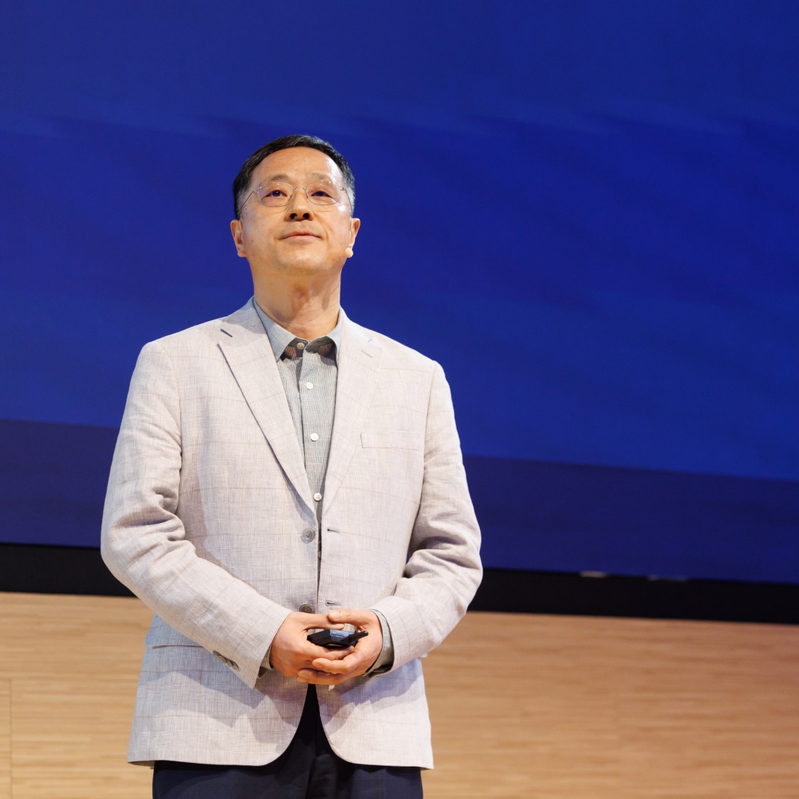 A speaker in a light gray blazer standing on stage with a blue background