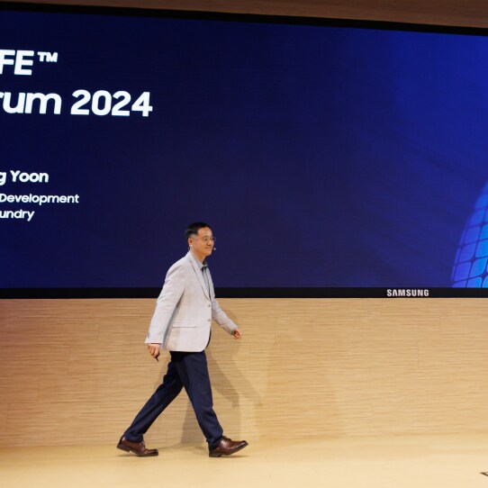 A presenter walking on the SAFE™ Forum 2024 stage with the event name displayed on the screen