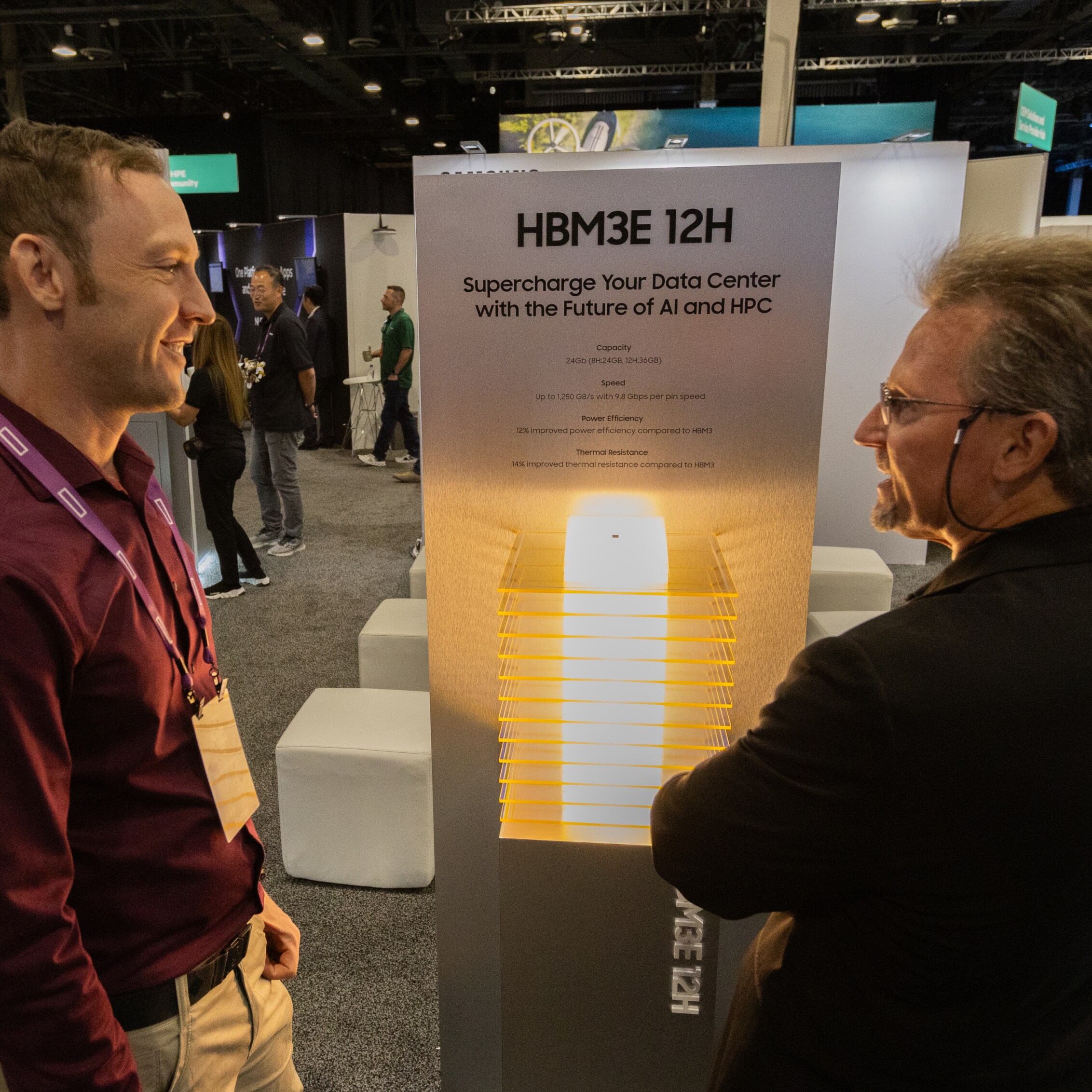 Two men discussing the HBM3E 12H technology display at HPE Discover 2024, emphasizing its high capacity and efficiency for AI and HPC.