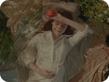 A Young girl lying on the grass, playfully balancing a red apple on her arm