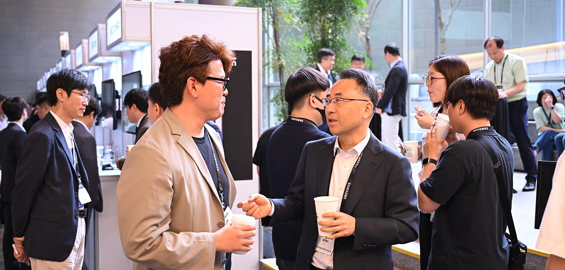 Attendees at a Samsung event engage in conversation and networking during a coffee break, holding cups and wearing name badges.