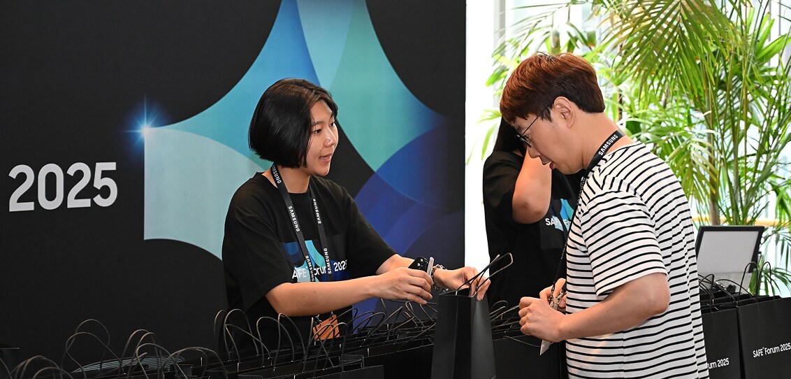A staff member hands a welcome gift bag to an attendee at the SAFE™ Forum 2025 registration desk, with branded packaging in the background.