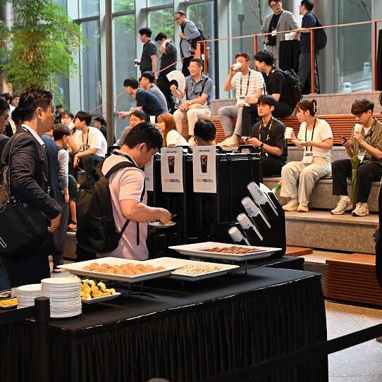 Attendees gather at a refreshment table during SAFE™ Forum 2025, enjoying coffee and pastries while seated in a modern, open lounge area.