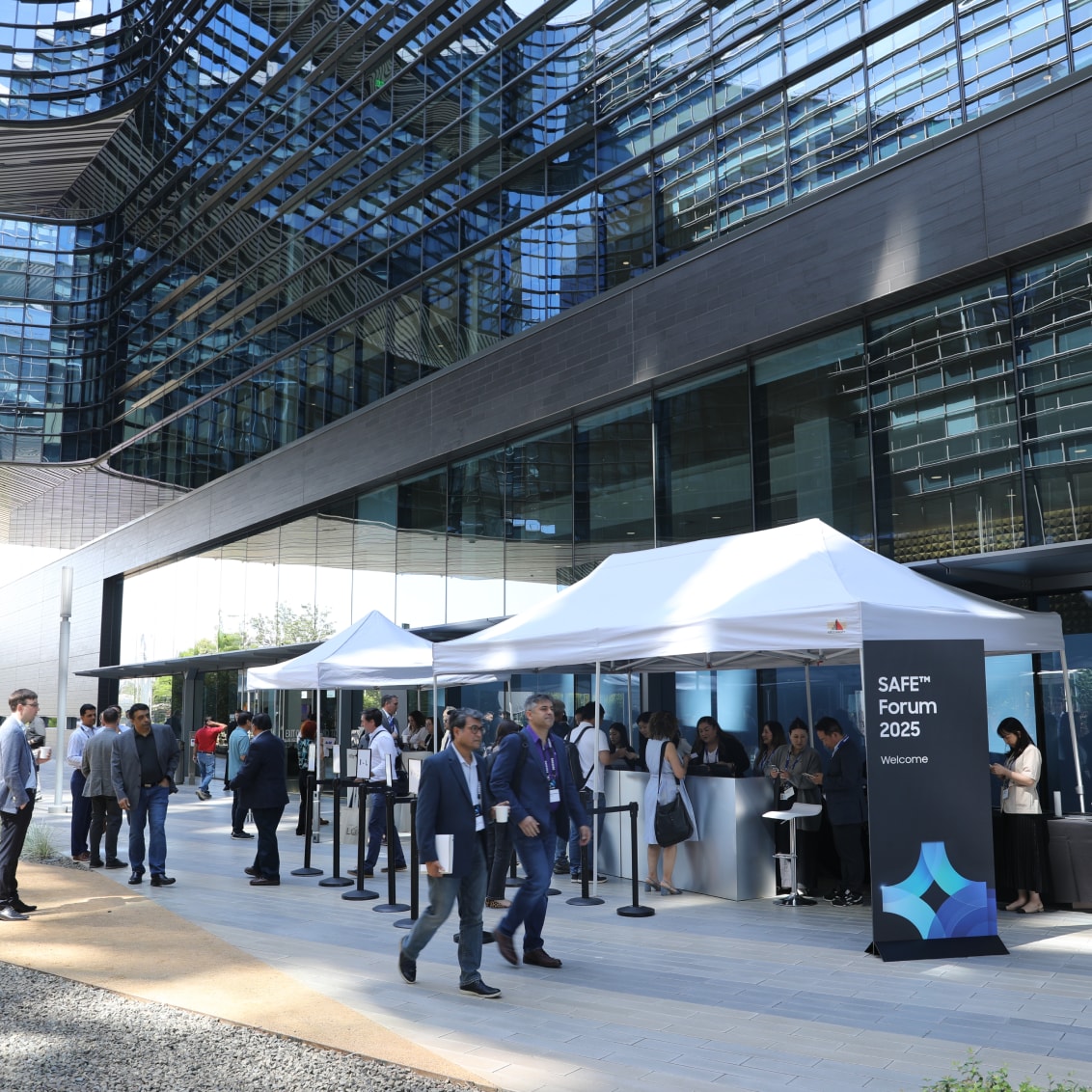 Attendees walk past check-in tents outside a modern glass building at the SAFE™ Forum 2025.