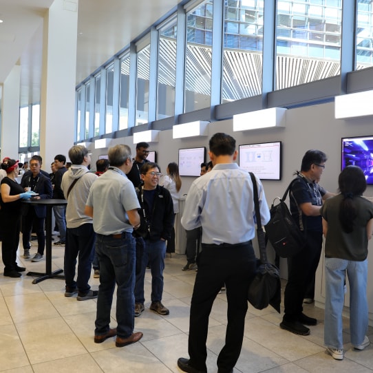 Attendees explore interactive digital displays at the SAFE™ Forum 2025, engaging in discussions along a well-lit hallway with large windows.