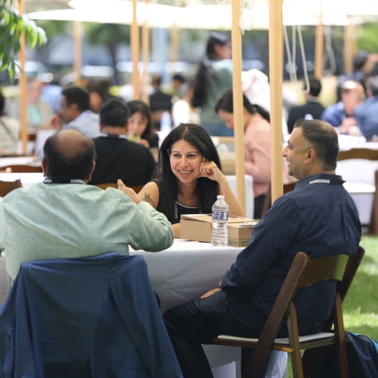 Attendees of the SAFE™ Forum 2025 enjoy a casual outdoor lunch under canopy tents, engaging in friendly conversation around a white-cloth