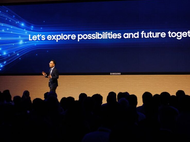 A Samsung keynote speaker presents on stage in front of a large screen displaying the message “Let’s explore possibilities and future together.”