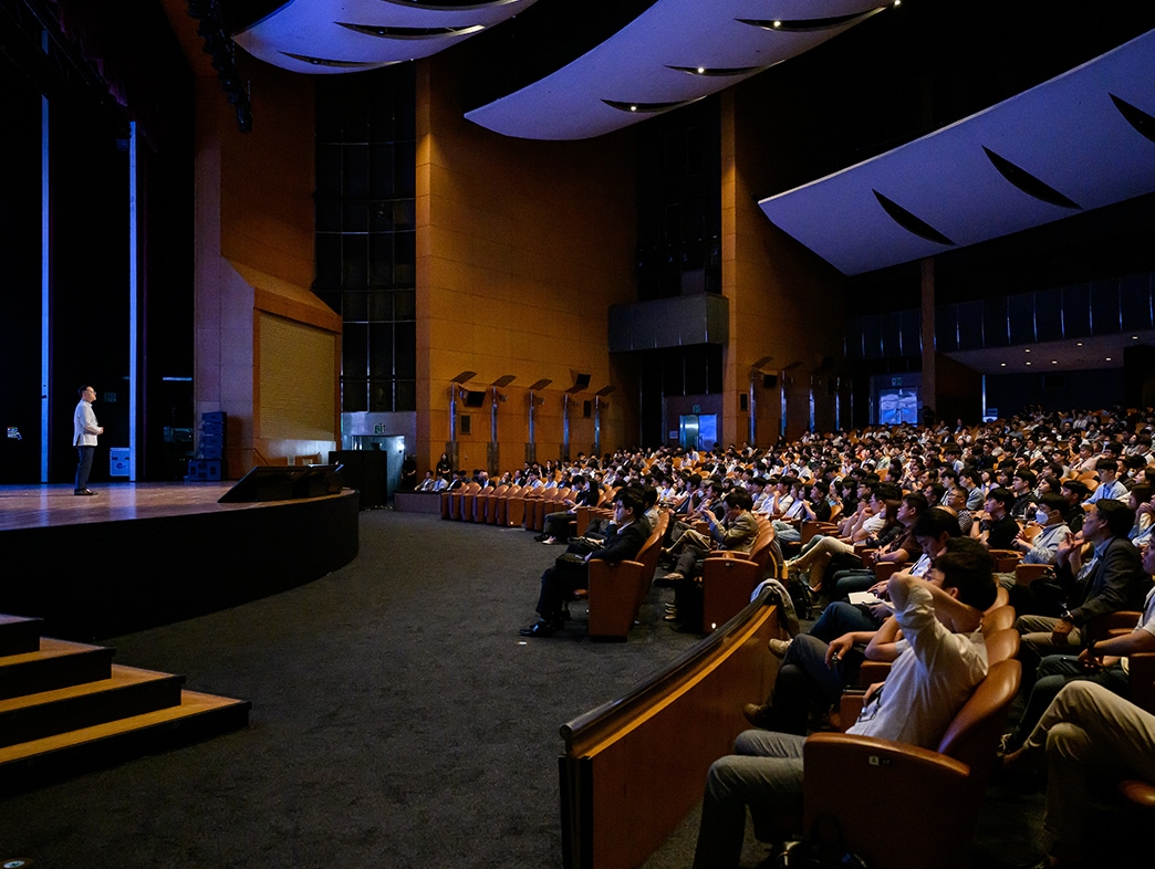 Speaker presenting on stage to a large audience in an auditorium at a technology conference.