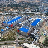 Aerial view of an expansive semiconductor manufacturing complex, featuring multiple large blue-roofed buildings and surrounding infrastructure.