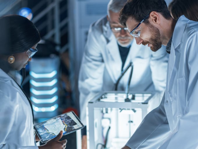 A group of scientists in a lab, collaboratively discussing over a tablet.