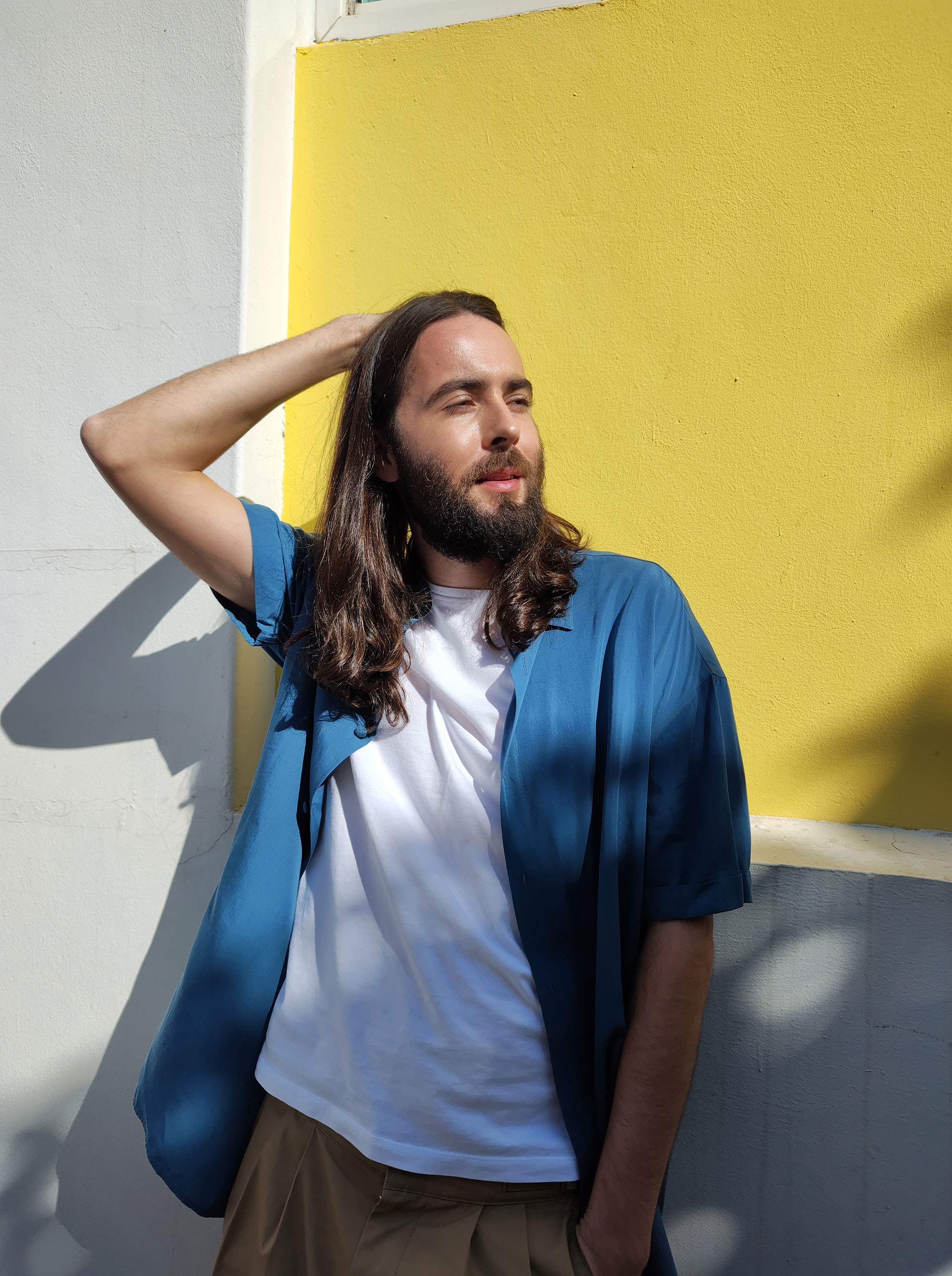  a casual man with long brown hair is posing in the sunlight