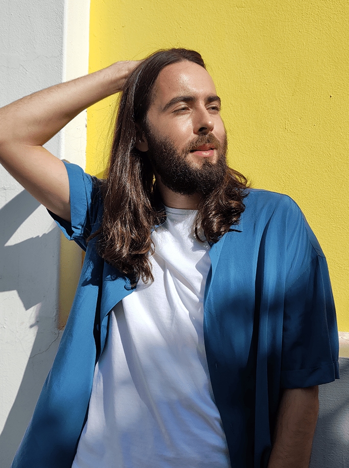  a casual man with long brown hair is posing in the sunlight
