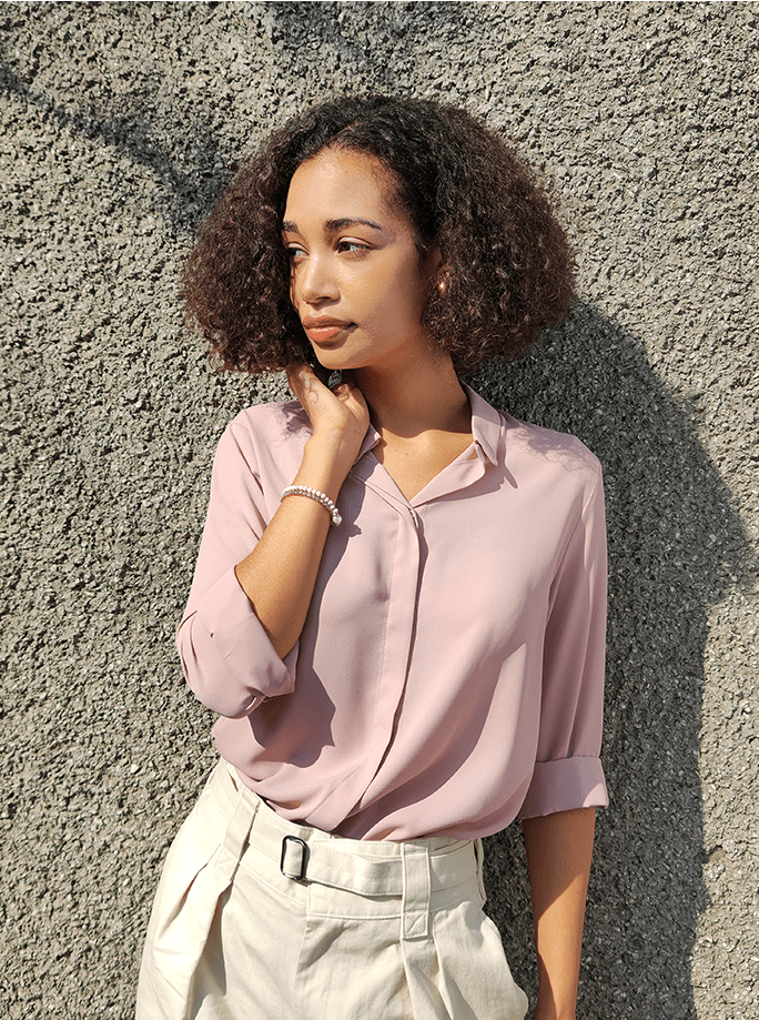  a woman with a pale pink shirt and skirt is posing and looking sideway 