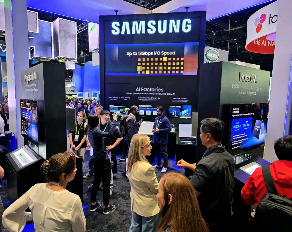 A bustling Samsung exhibition booth where visitors are exploring next-generation AI semiconductor technologies, featuring large displays highlighting "Up to 13Gbps I/O Speed", "AI Factories", and "Local AI".