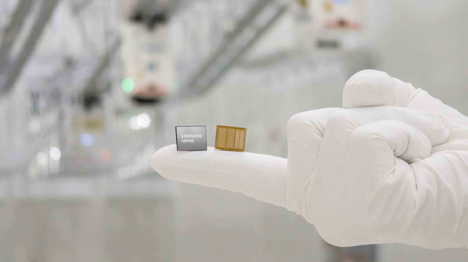 A Samsung HBM4E memory chip and a yellow circuit board placed on a gloved finger, with semiconductor manufacturing equipment blurred in the background.