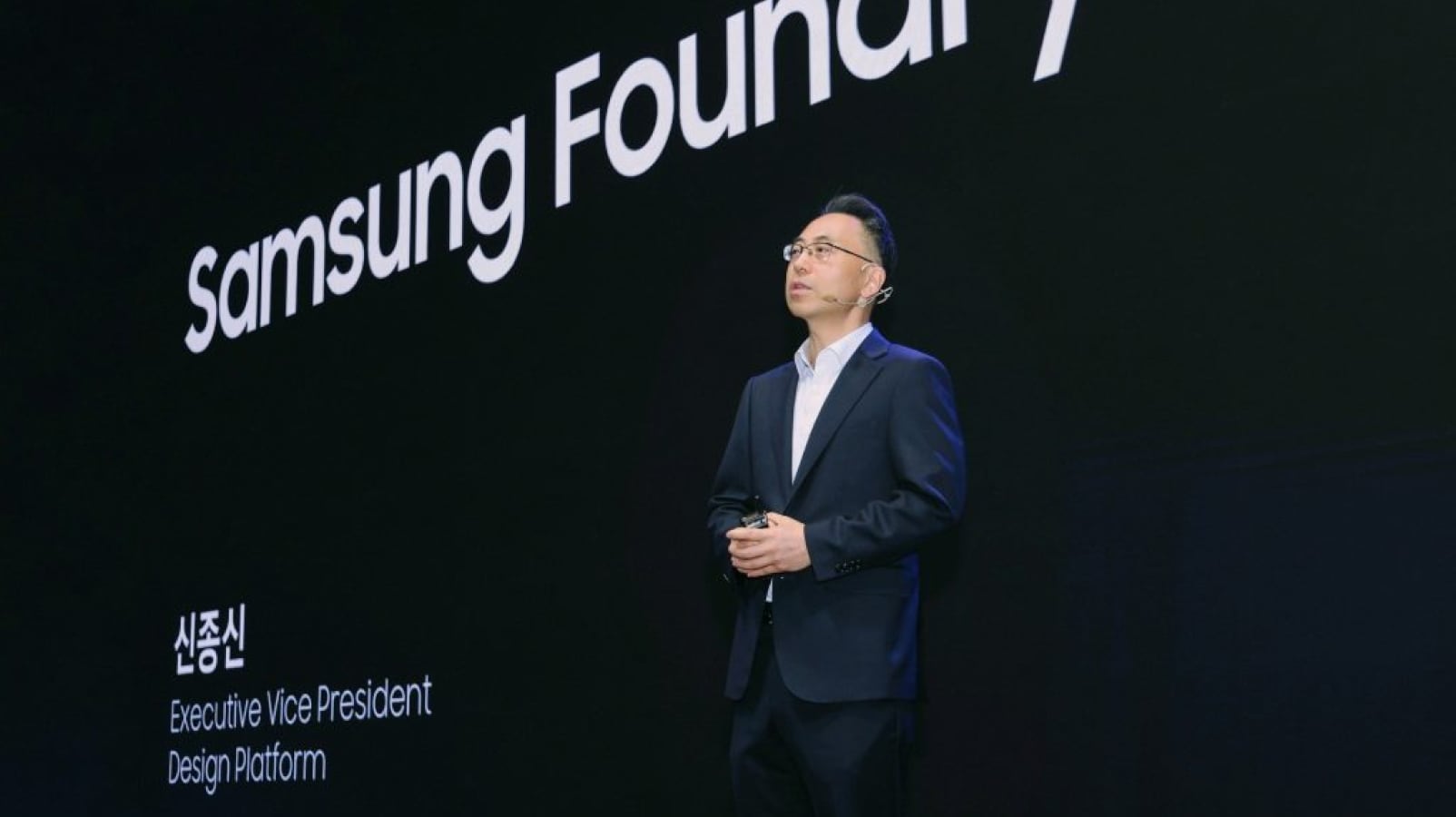 검은색 정장을 입은 남성 연사가 무대에서 발표를 하고 있으며, 그의 뒤에는 "Samsung Foundry"와 발표자의 직함 정보가 흰색 글씨로 표시되어 있습니다.