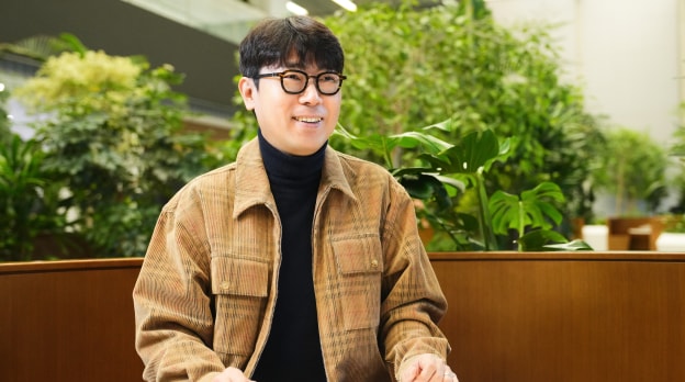 센서 설계 팀의 TL이 실내 녹지 공간에서 미소를 지으며 인터뷰에 응하고 있는 모습.