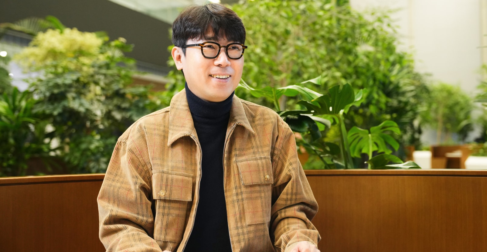 센서 설계 팀의 TL이 실내 녹지 공간에서 미소를 지으며 인터뷰에 응하고 있는 모습.