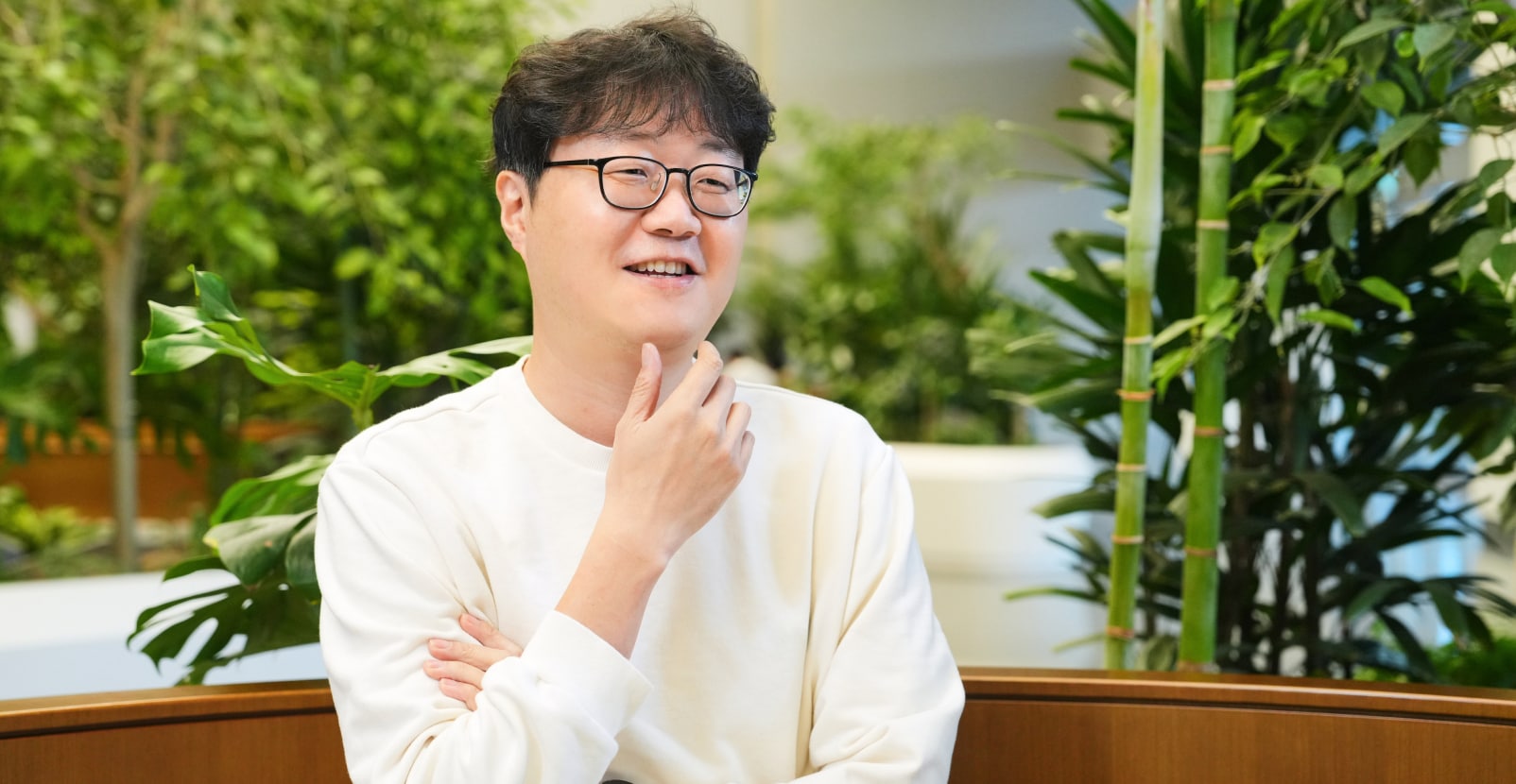 센서 PA 팀의 TL이 실내 녹지 공간에서 턱에 손을 올린 채 미소를 지으며 인터뷰 중인 모습.