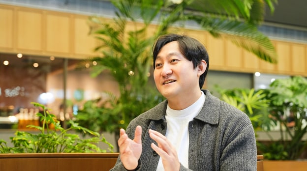 Security&Power제품개발팀의 김지철 님이 자연스러운 손짓과 미소로 대화를 나누는 모습으로, 따뜻한 톤의 실내 공간 분위기를 담음