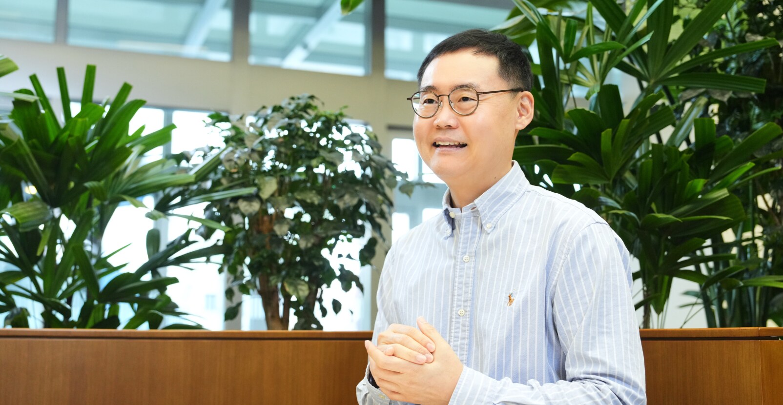 Security&Power제품개발팀의 유승택 TL이 안경을 쓰고 스트라이프 셔츠를 입은 채 관엽식물이 있는 사무공간에서 밝은 표정으로 설명하는 모습