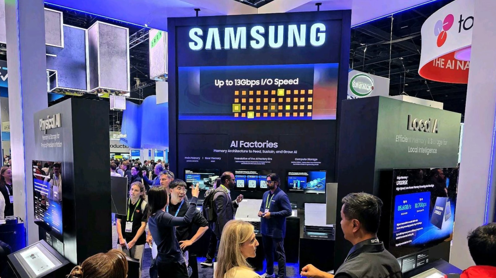 A bustling Samsung exhibition booth where visitors are exploring next-generation AI semiconductor technologies, featuring large displays highlighting "Up to 13Gbps I/O Speed", "AI Factories", and "Local AI".