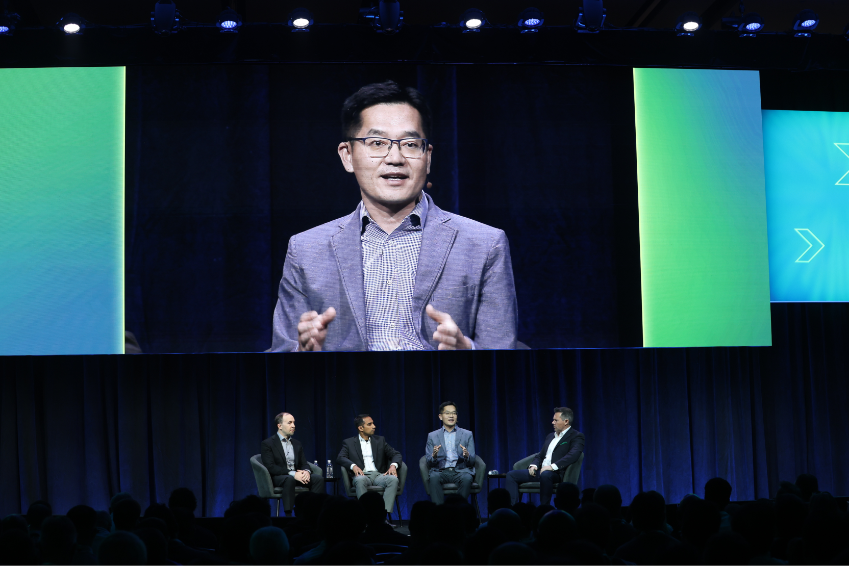 A panel discussion at the 2024 OCP Global Summit, with four experts on stage and a large screen displaying a close-up of one speaker..