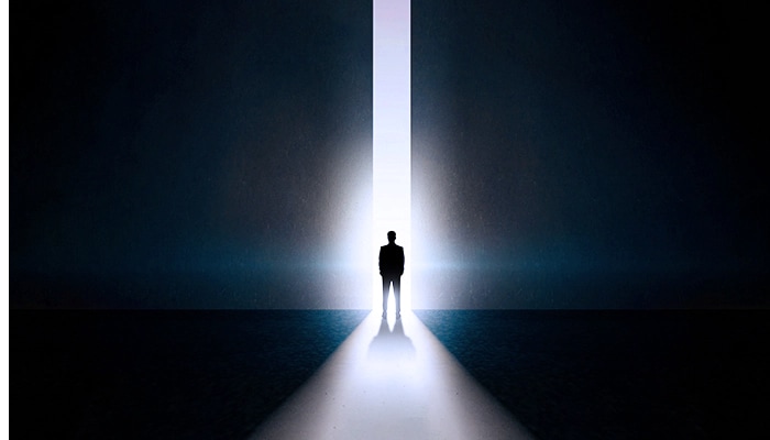Under a dark background, you can see a man turning around in front of a huge open door. And there's a light coming out of the door, which makes the man stand out.