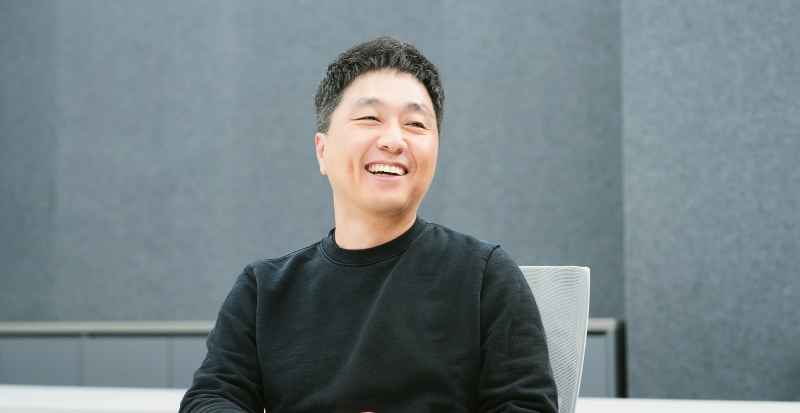 회의실에서 책상 앞에 앉아 미소를 짓는 남성.