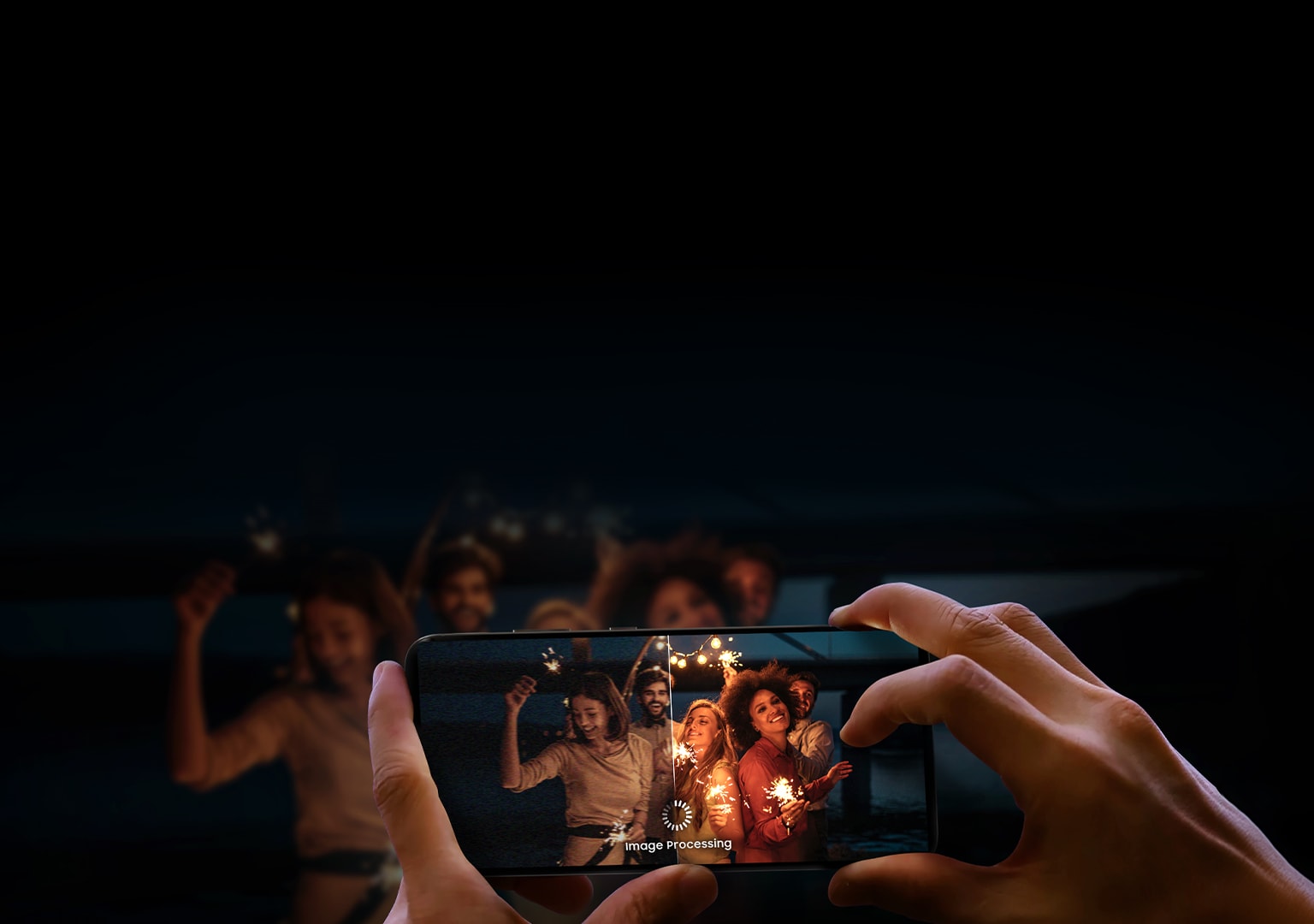 A person holds a smartphone capturing a group of people celebrating at night, emphasizing the phone's low-light photography and image processing capabilities.