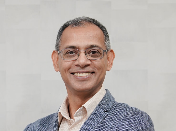 Professional portrait of Anshul Sharma, Head of Memory Solutions, wearing a textured blazer and glasses, smiling with arms crossed against a light patterned background.
