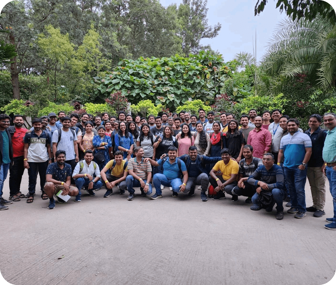A large team of professionals posing outdoors for a group photo, surrounded by lush greenery and trees.