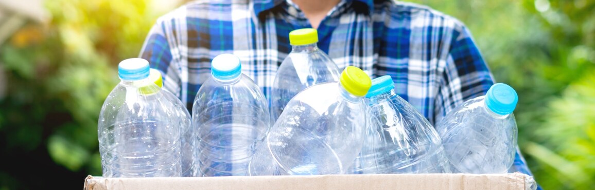 チェック柄のシャツを着た人が、さまざまな色の蓋のある空のプラスチックの瓶を箱に入れてリサイクルを準備しています。
