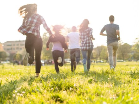 A group of people running across a wide lawn under warm sunlight